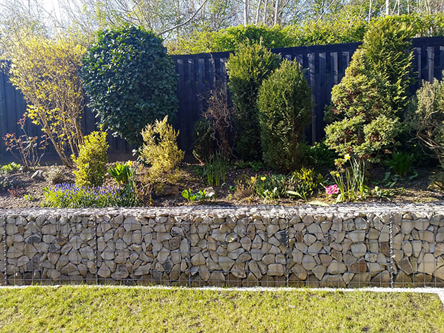 Paniers de gabions retenant un massif de buissons et de fleurs